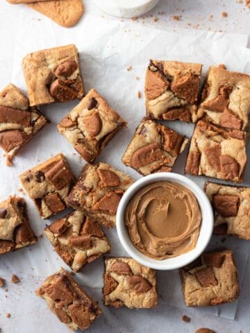 Biscoff blondies cut into square with a small bowl of cookie butter spread and a glass of milk.