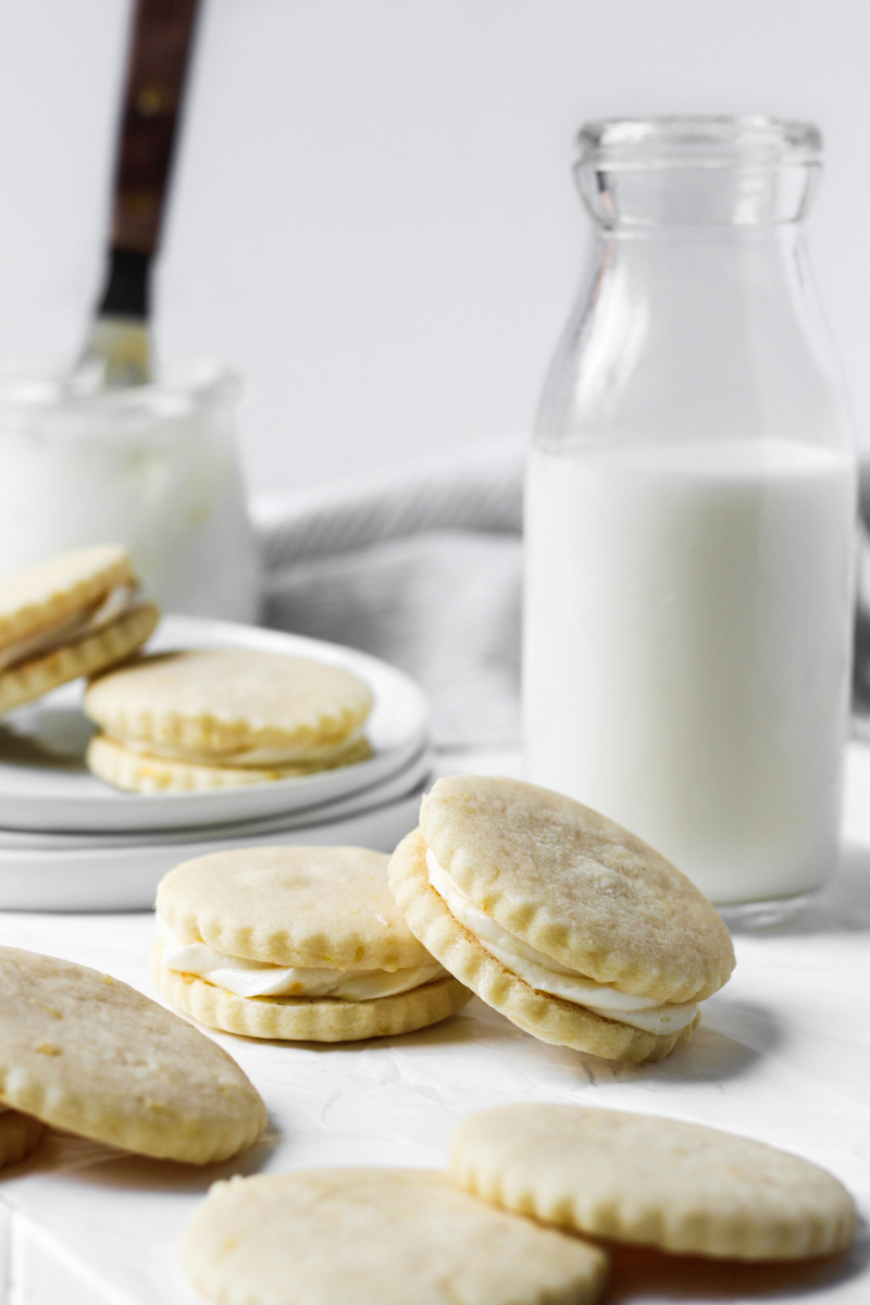 Lemon butter cookie sandwiches with lemon buttercream and a glass of milk.