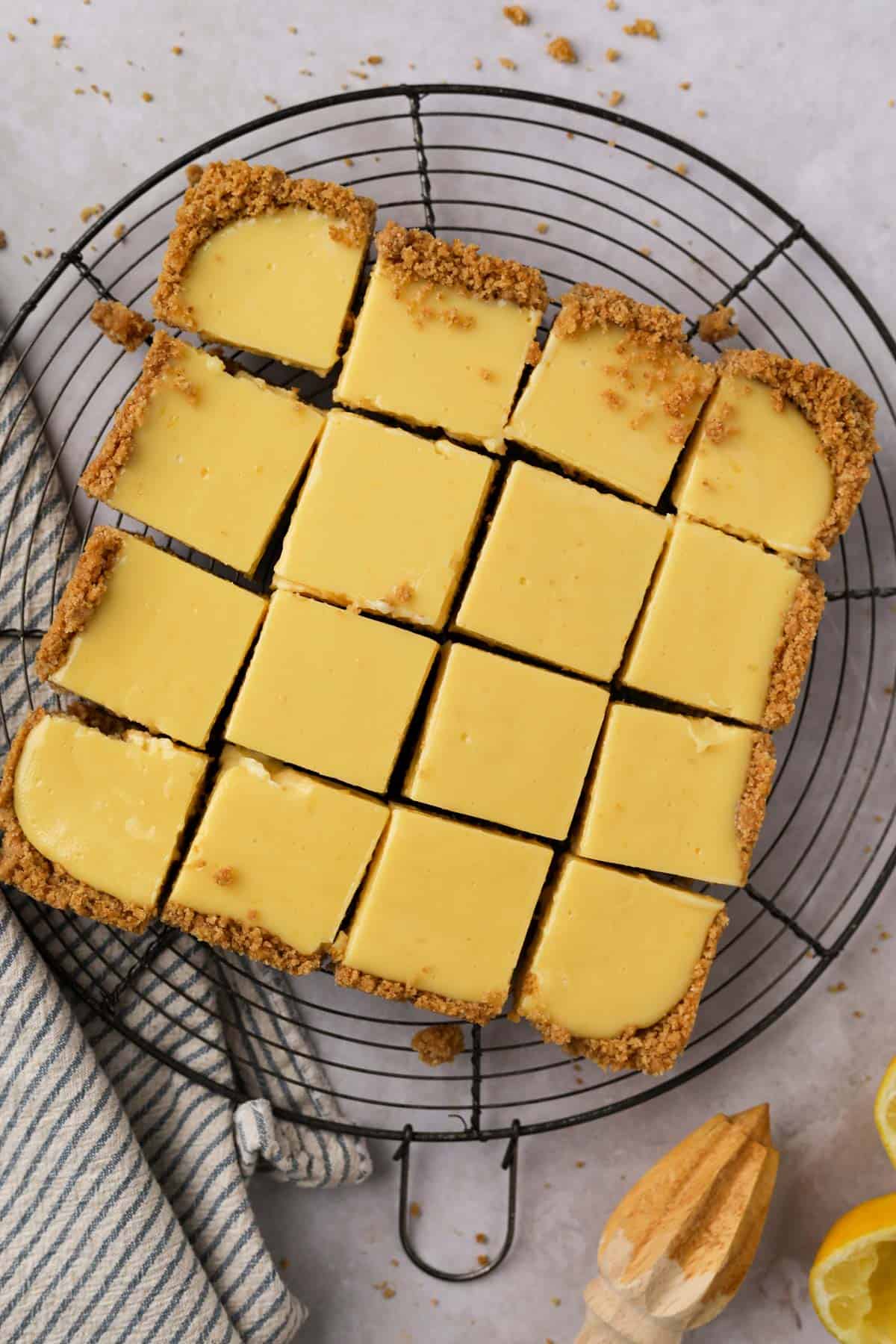 Baked lemon bars with graham cracker crust cut into 16 squares set over a round wire cooling rack.
