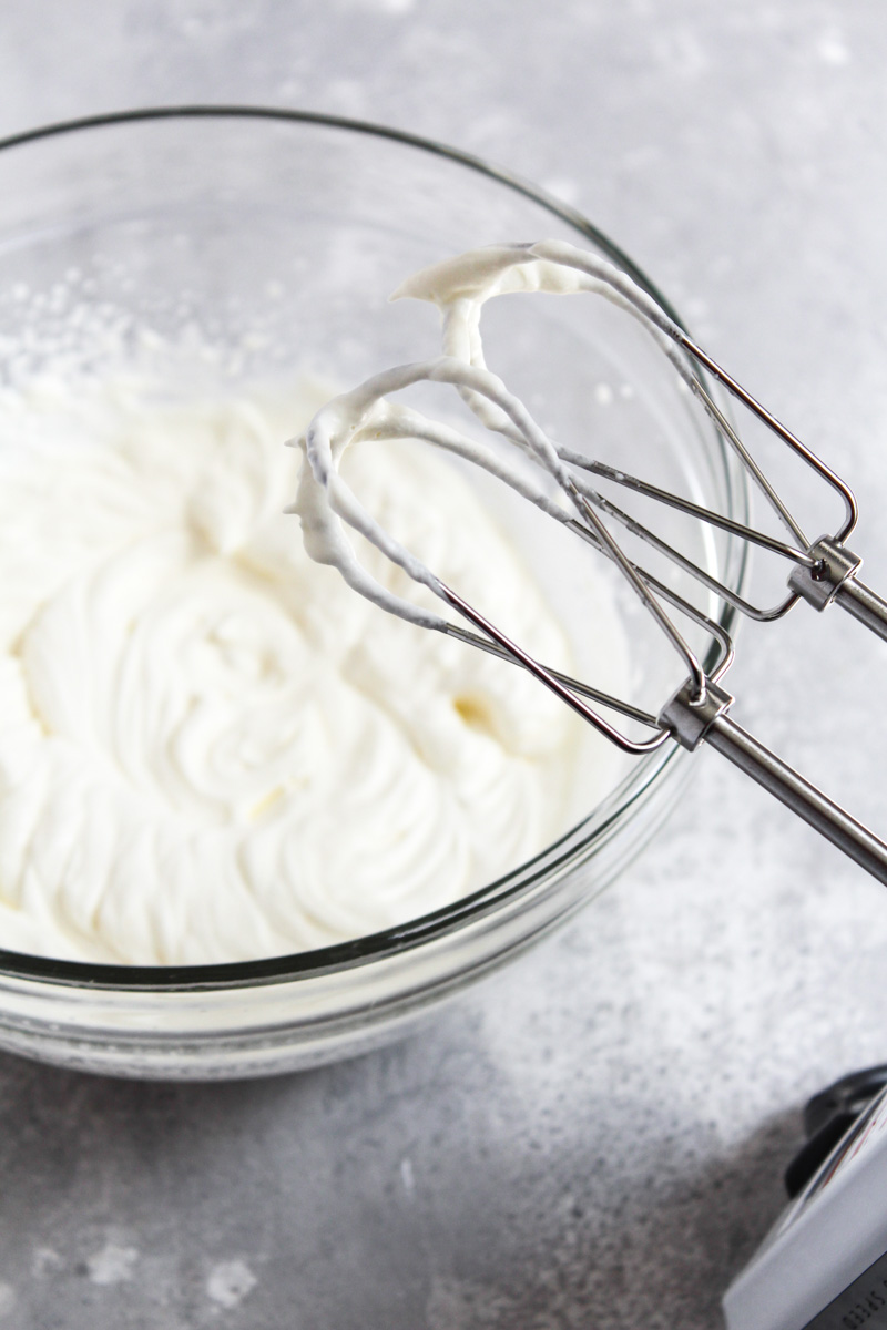 Bowl of homemade whipped cream with beaters displaying medium peaks