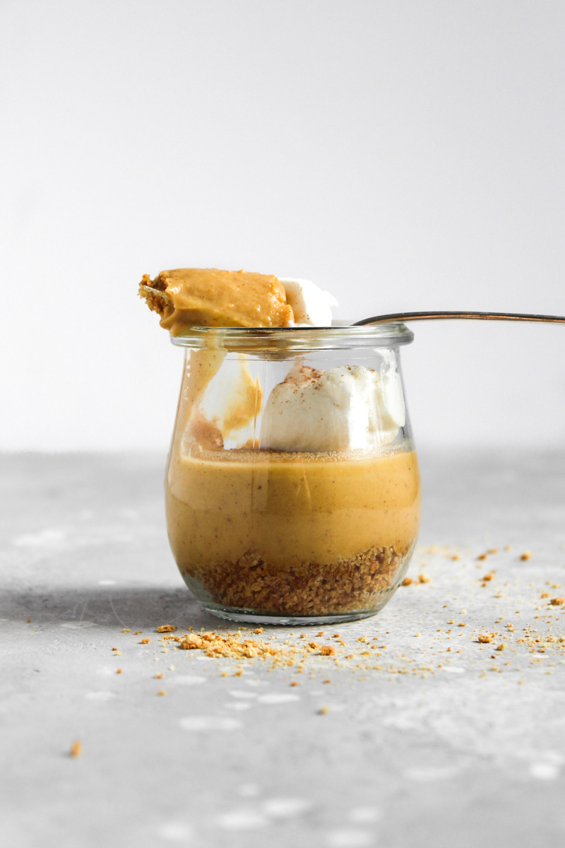 Side shot of pumpkin custard in a glass jar with a spoon of the custard laying on top of the jar.