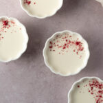 Refrigerated and set coconut panna cotta in molds sprinkled with freeze-dried raspberry powder.