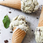 Three sugar cones of mint chocolate chip ice cream on their side.