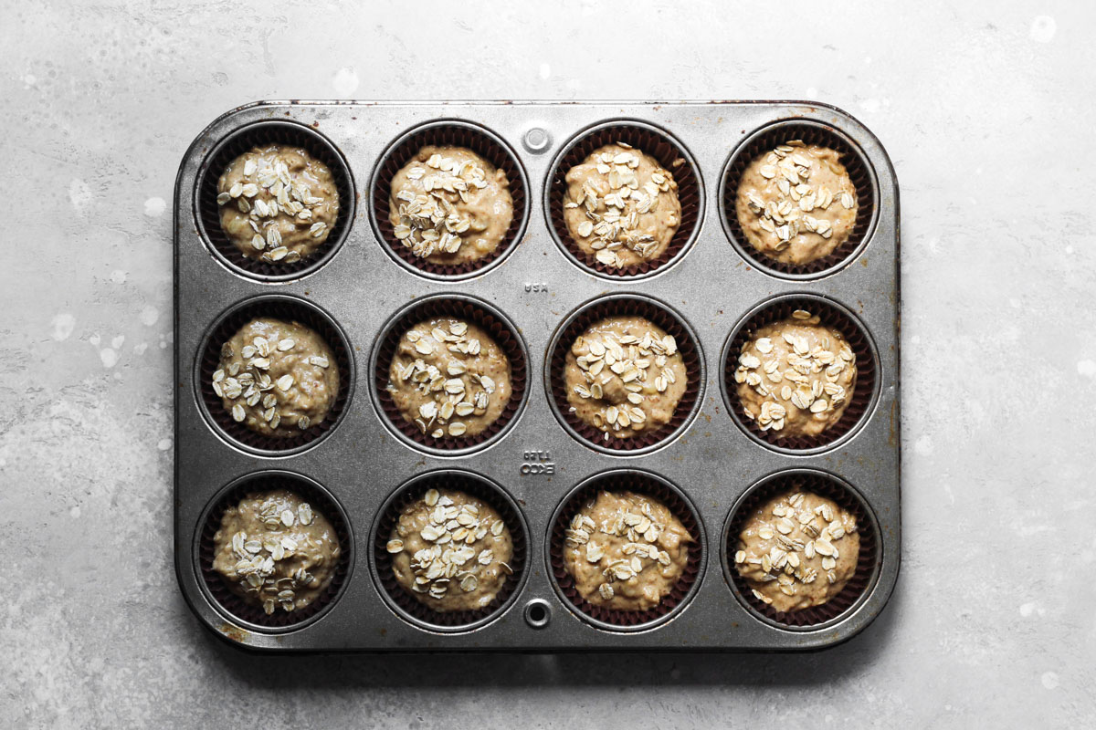 Batter portioned into muffins tins for banana muffins topped with raw oats.