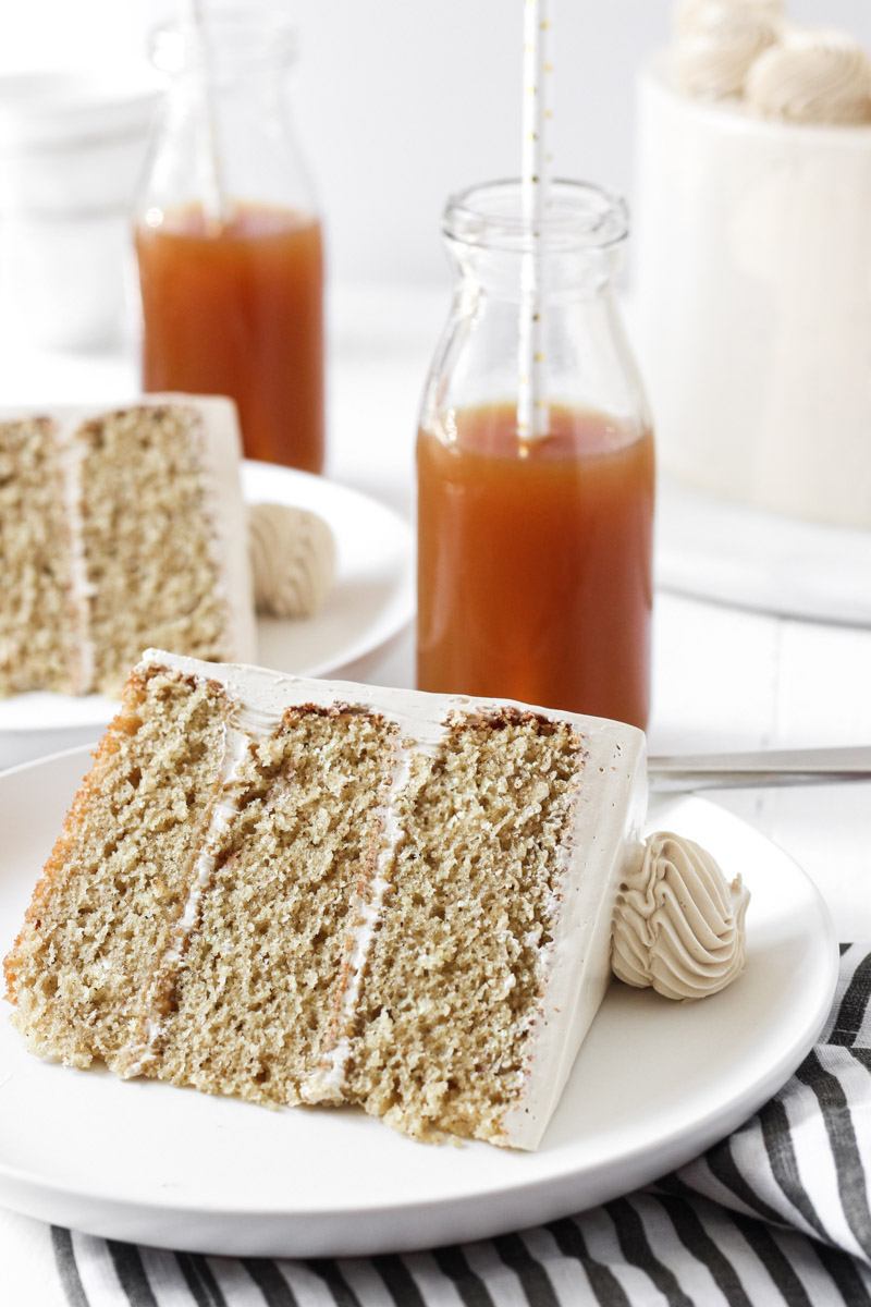 Two slices of apple cider cake on plates with apple cider in the backgroud.