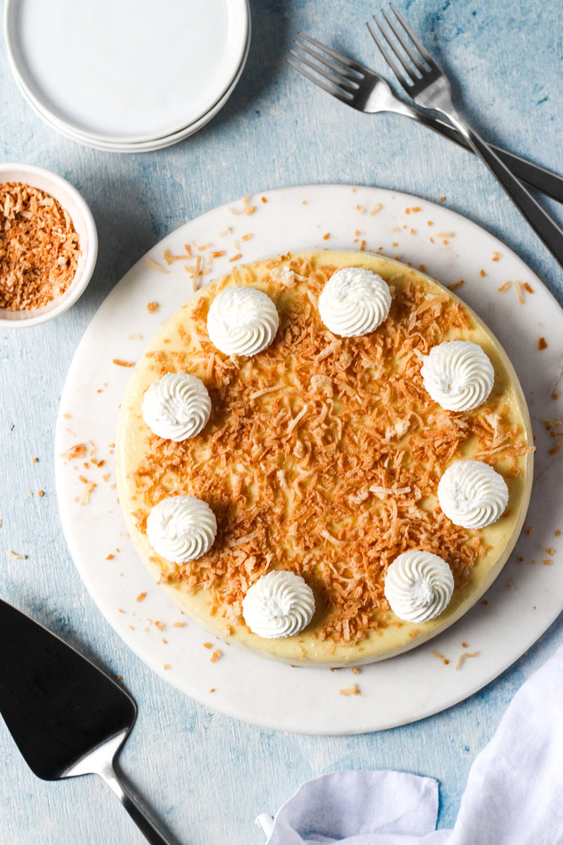 Overhead view of coconut cheesecake with a layer of toasted coconut and dollops of whipped cream.