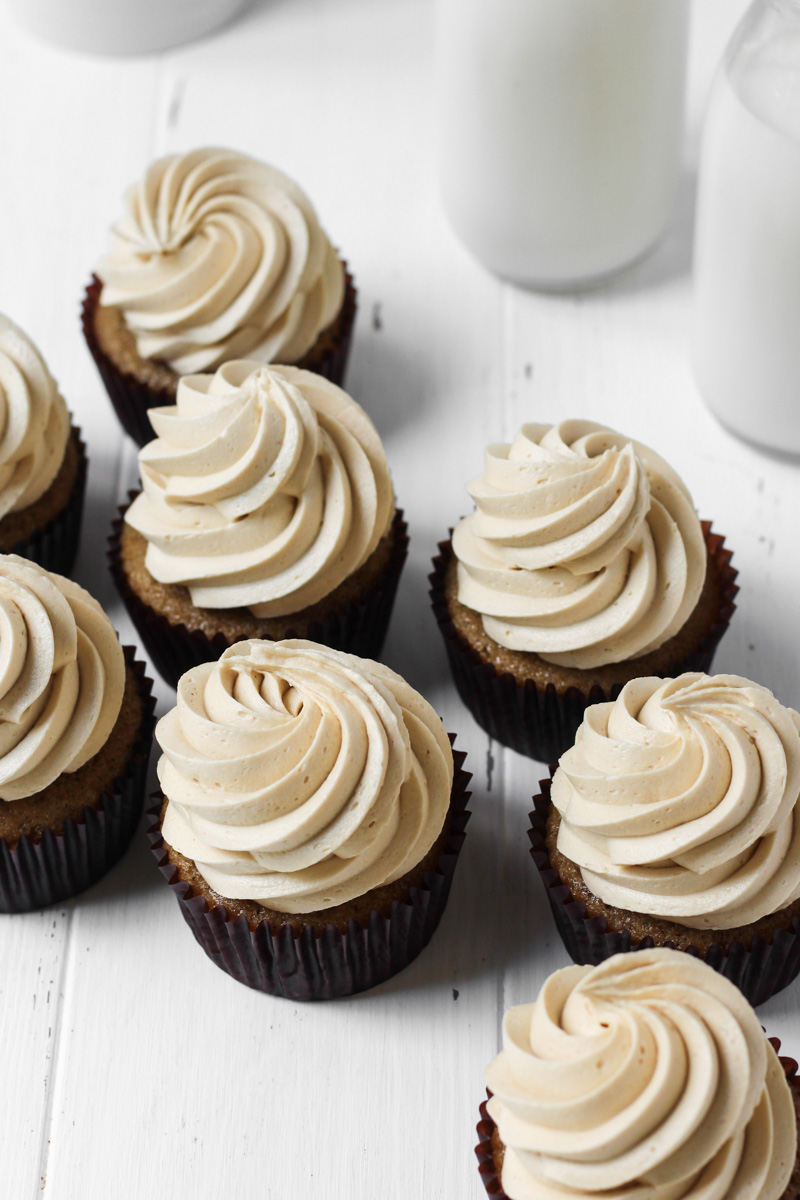 Several coffee cupcakes with coffee buttercream on a white wood board for display.