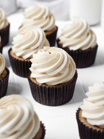 Several coffee cupcakes with coffee buttercream on a white wood board for display.