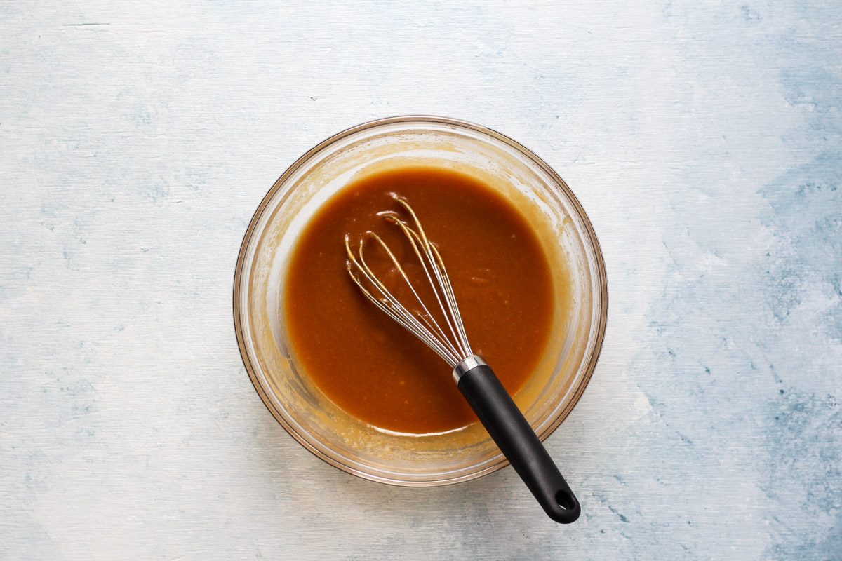 Glass bowl of mixed wet ingredient with whisk for cookie butter cookies.