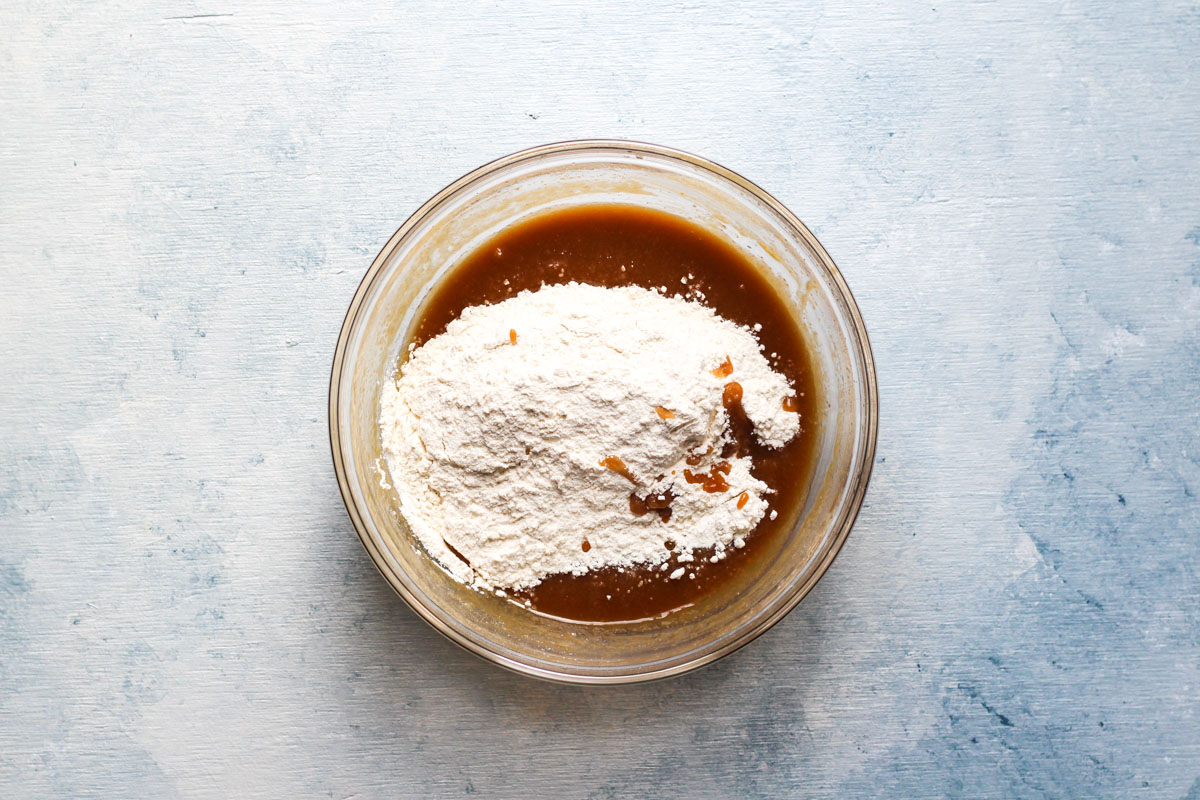 Glass bowl with cookie butter cookie wet ingredients topped with dry ingrdients.