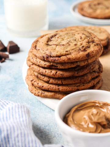 Stack of cookie butter cookies with bowl of cookie butter and glass of milk.