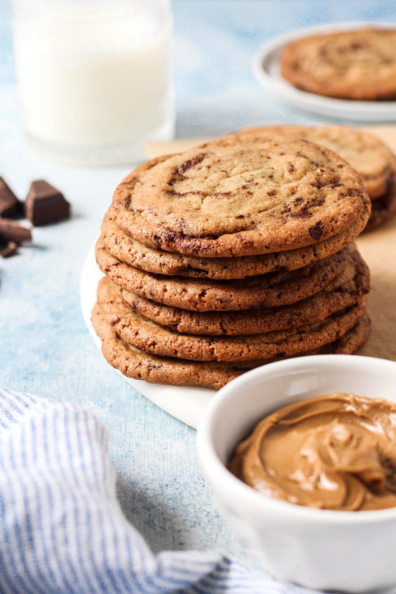 Stack of cookie butter cookies with bowl of cookie butter and glass of milk.