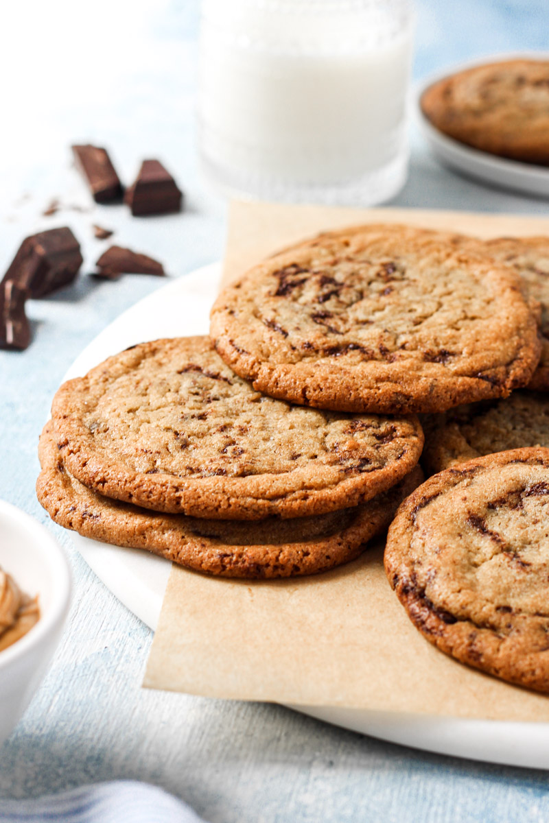 Cookie butter cookies arranged on marble round and parchment paper with glass of milk and chocolate chunks in background.