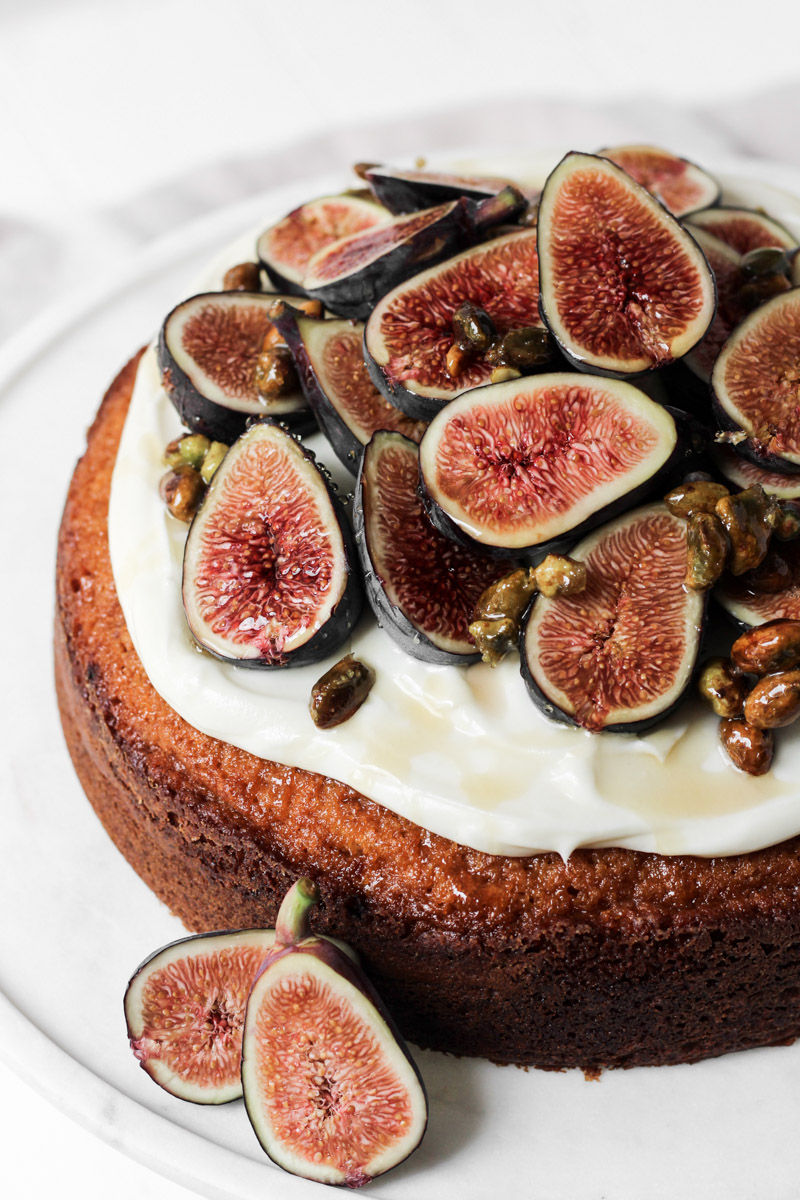 Close up of fig cake with fresh seasonal figs, cream cheese frosting, honey and nuts on a cake stand.