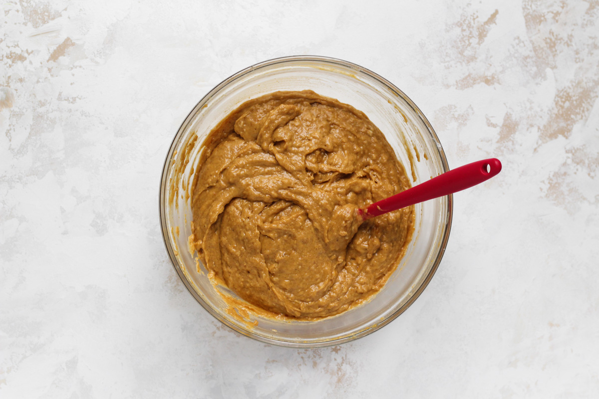 Pumpkin donut batter in a glass bowl with a red spatula.