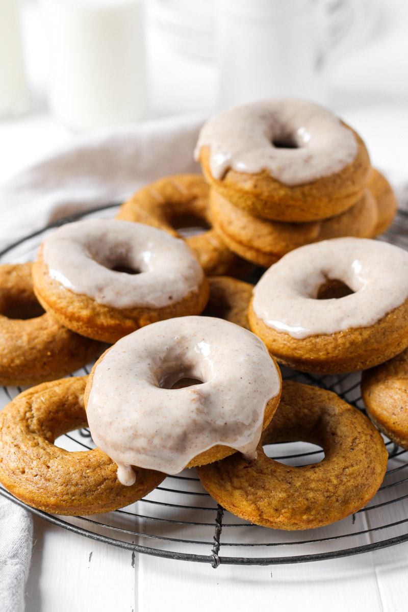 Stack of baked pumpkin donuts some with glaze on a round French wire rack.