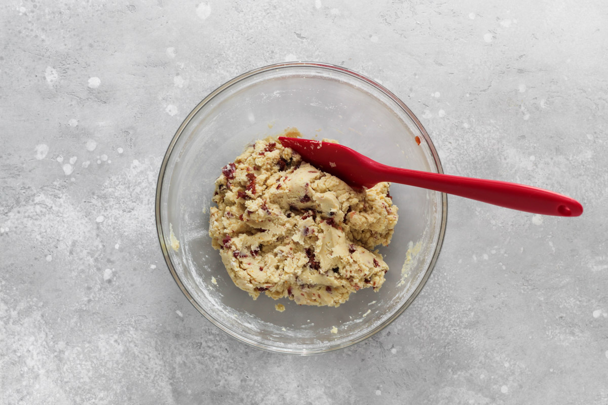 Cranberry orange shortbread cookie dough in a glass bowl with a red spatula.