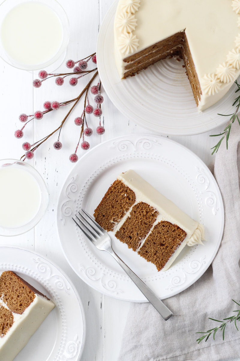 Overhead shot of gingerbread layer cake with two slices on a plates and the cake on a white cake stand.