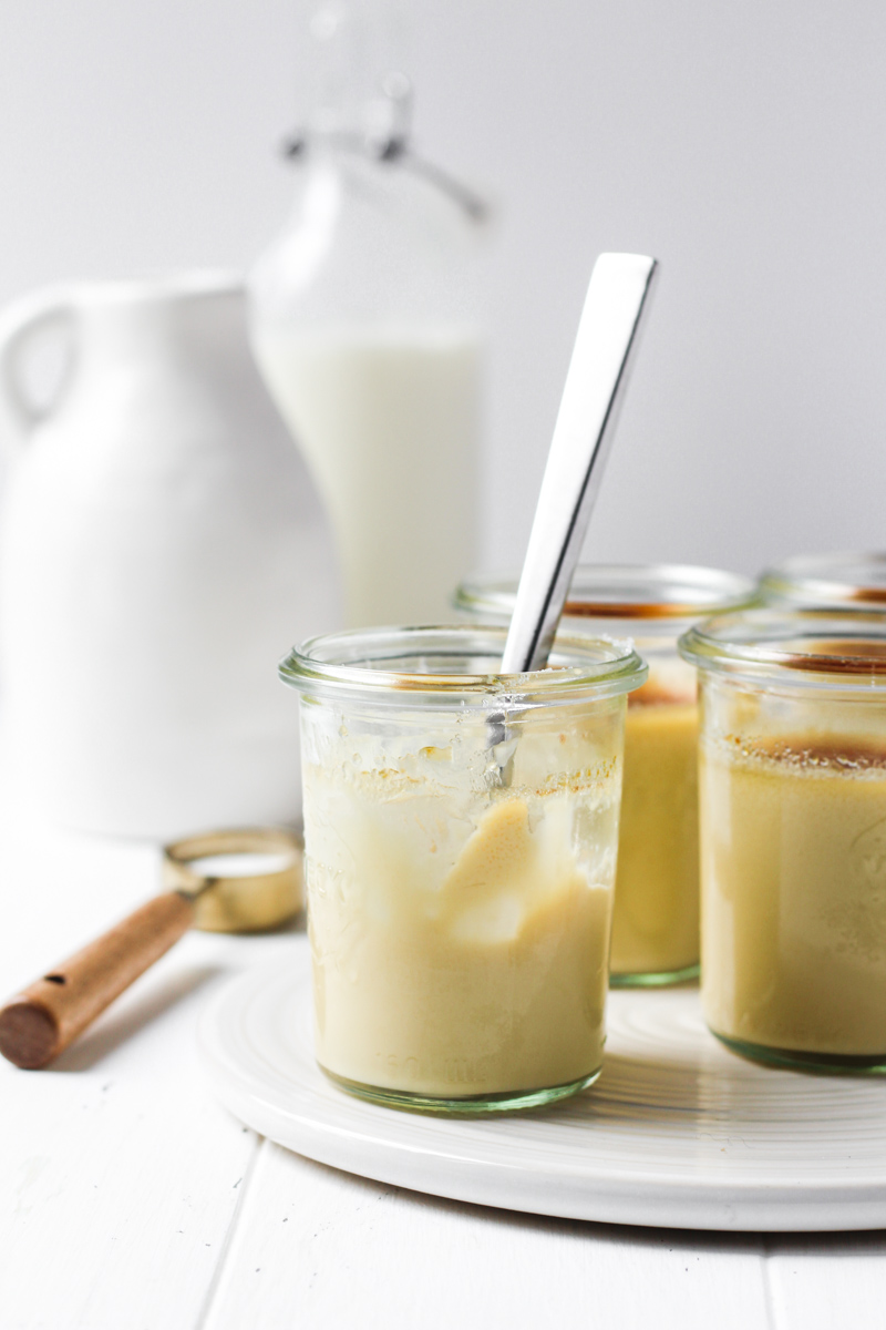 Glass jars of maple creme brulee with one half finished with a spoon in the jar.