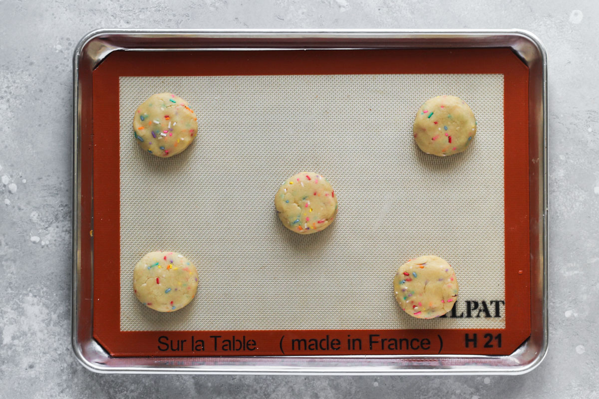 Sheet pan with 5 unbaked funfetti cookies stuffed with buttercream.