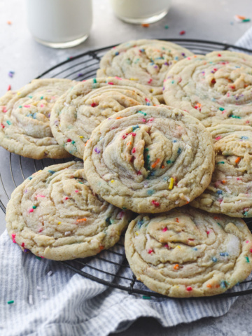 Stack of funfetti stuffed cookies with buttercream on a French wire rack.