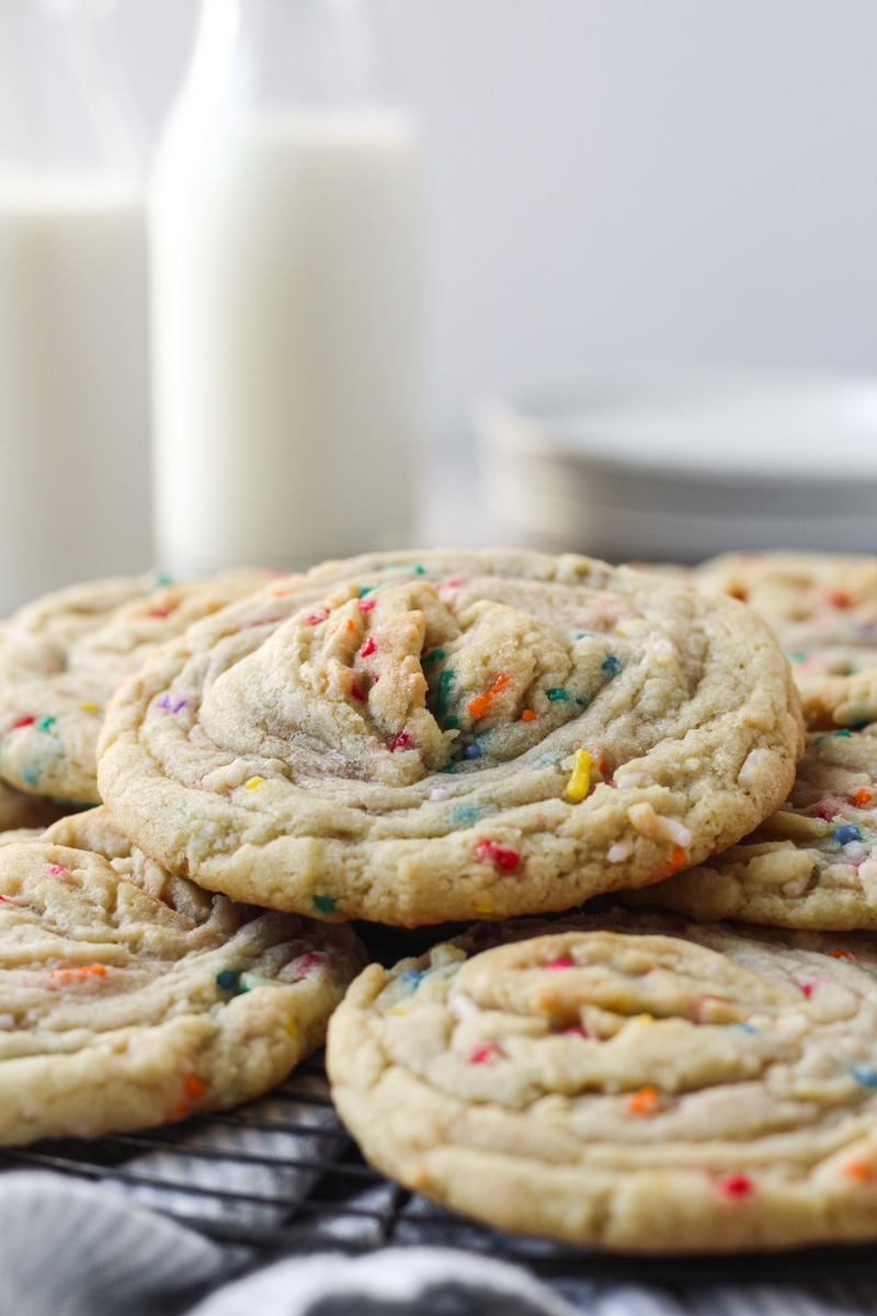 Stack of funfetti stuffed cookies with buttercream with milk and dishes in the background.