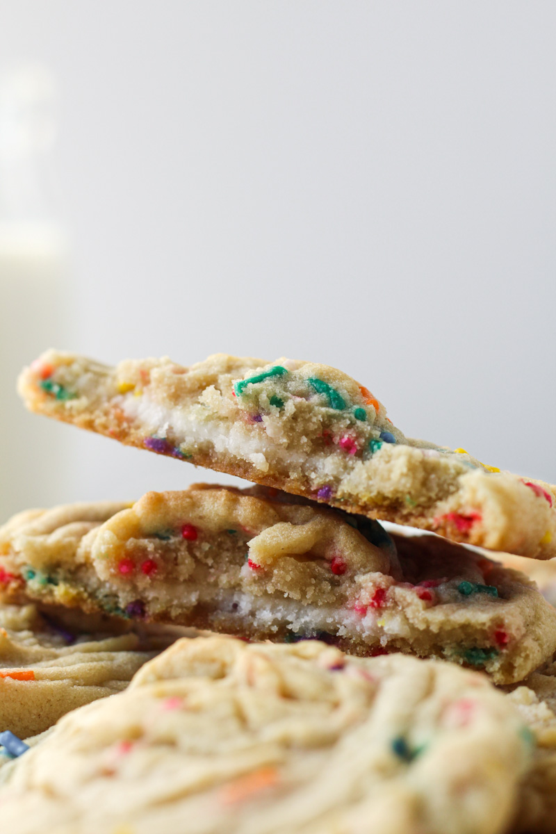 Stack of funfetti stuffed cookies with buttercream with cookie broken in half showing the filling.