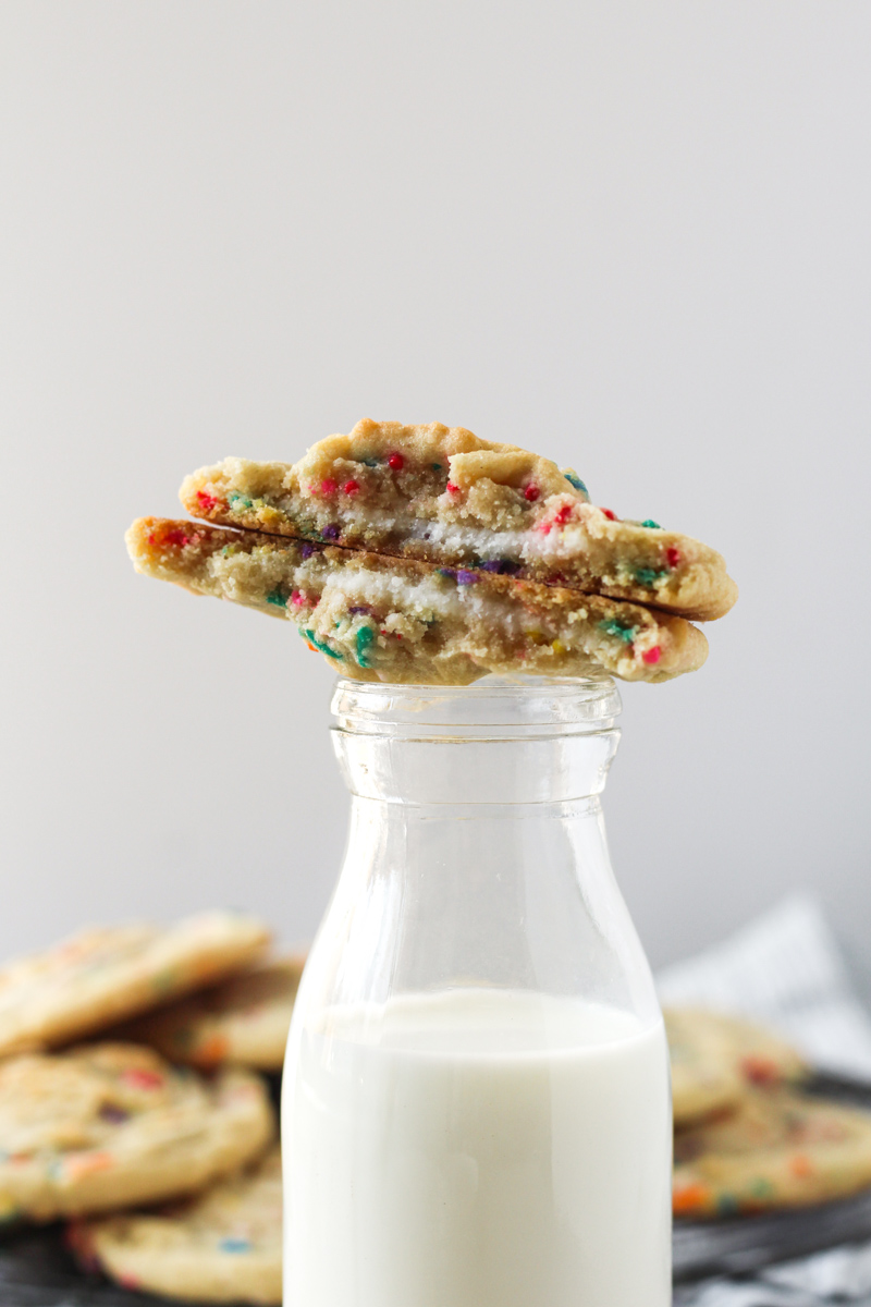 Funfetti cookies stuffed with buttercream broken in half and stacked on top of a glass of milk.