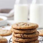 Stack of brown butter cookies with toffee bits on a French wire cooling rack with milk in the backgroud.