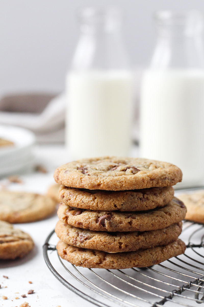 Stack of brown butter cookies with toffee bits on a French wire cooling rack with milk in the backgroud.