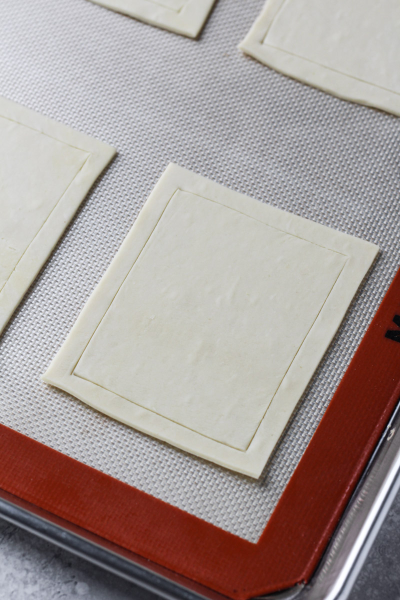 Puff pastry with a scored border on a baking sheet.