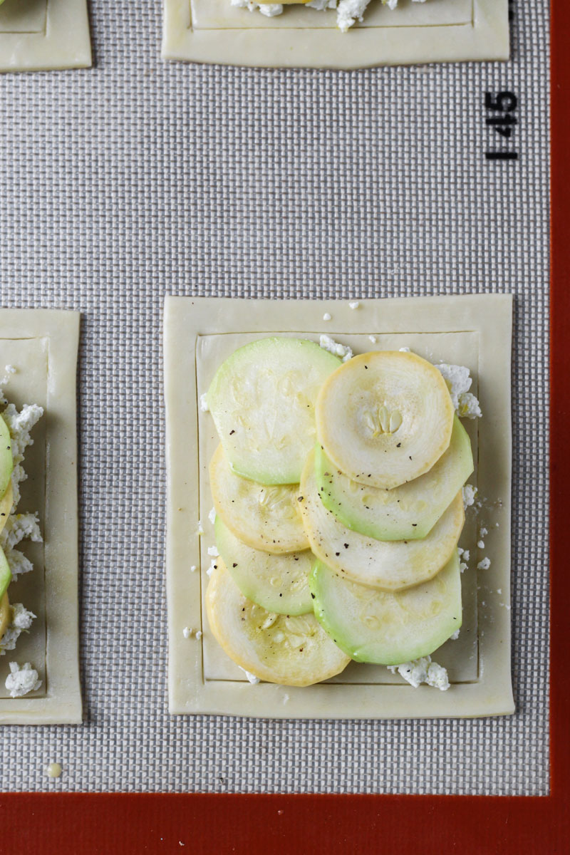 Puff pastry topped with feta and green and yellow zucchini on a baking sheet.