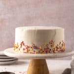8 Inch cake on a cake stand with sprinkles around the bottom edges.