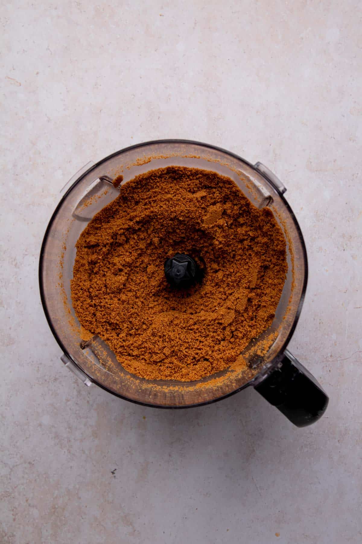 Biscoff cookies pulsed to a fine crumb in a food processor container set on a flat surface.