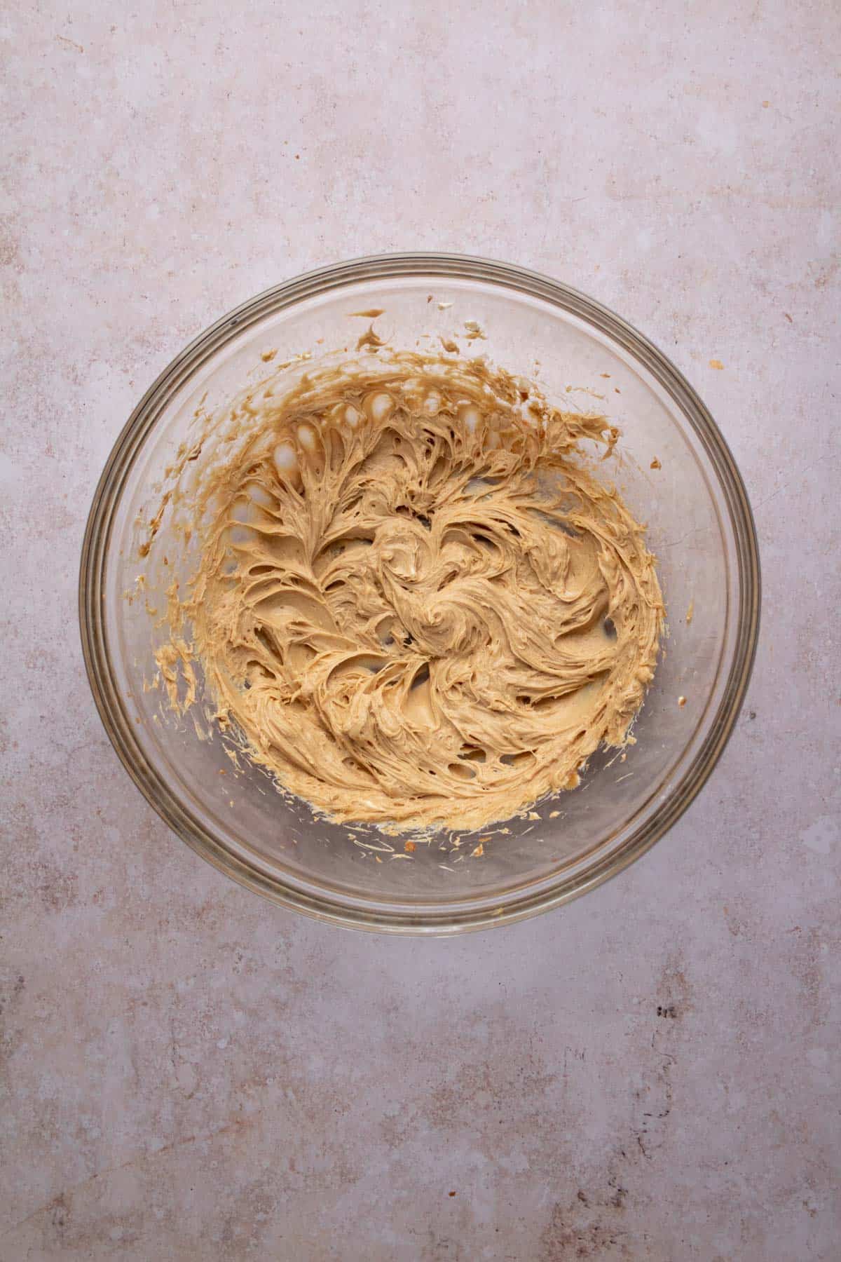 Cream cheese and Biscoff spread beaten together in a glass mixing bowl set on a flat surface.