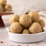 Biscoff truffles coated in a white chocolate cookie butter coating stacked in a white bowl.