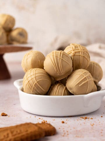 Biscoff truffles coated in a white chocolate cookie butter coating stacked in a white bowl.