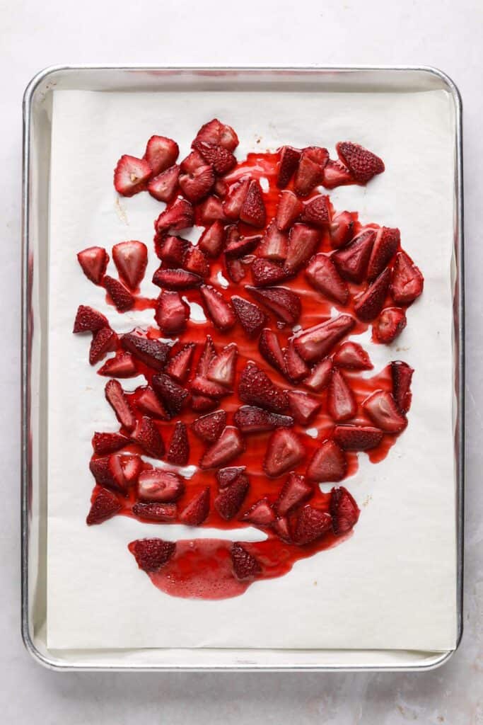 Roasted strawberries with their juices on a parchment lined sheet pan.