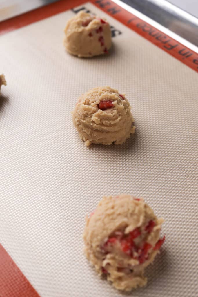 Silicone lined baking sheet with strawberry cheesecake cookie dough balls spread 3 inches apart.