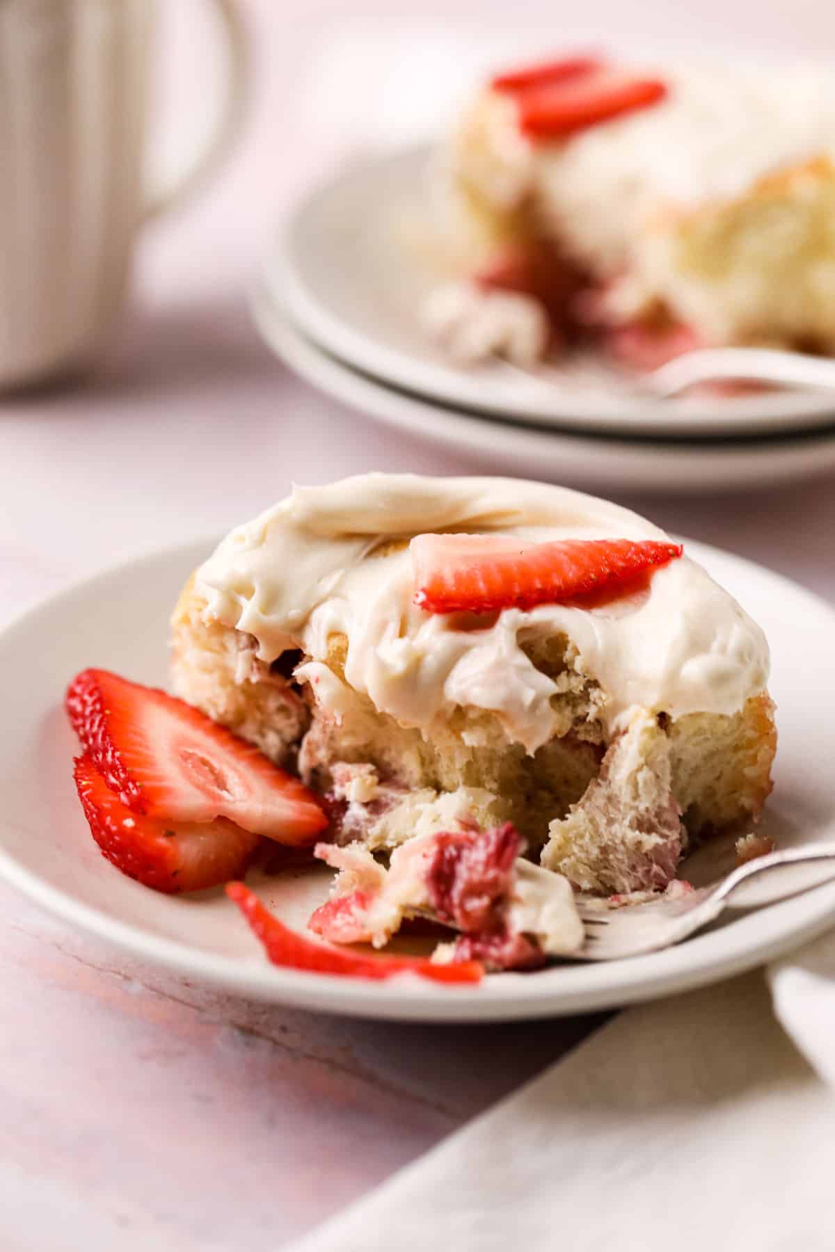 Dish with a fresh strawberry cinnamon rolls topped with fresh sliced strawberries and bite taken out of it.