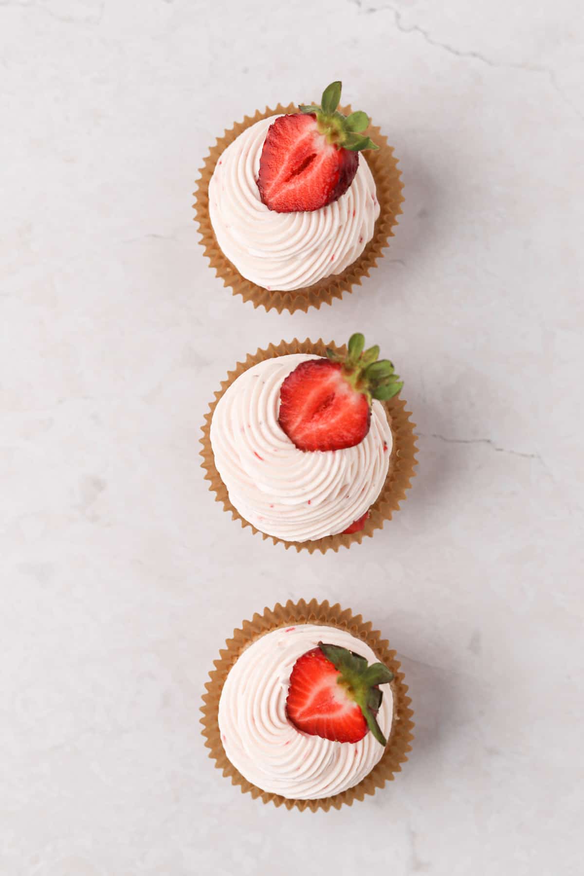 Three strawberry filled cupcakes with strawberry cream cheese frosting and a half strawberry for garnish.
