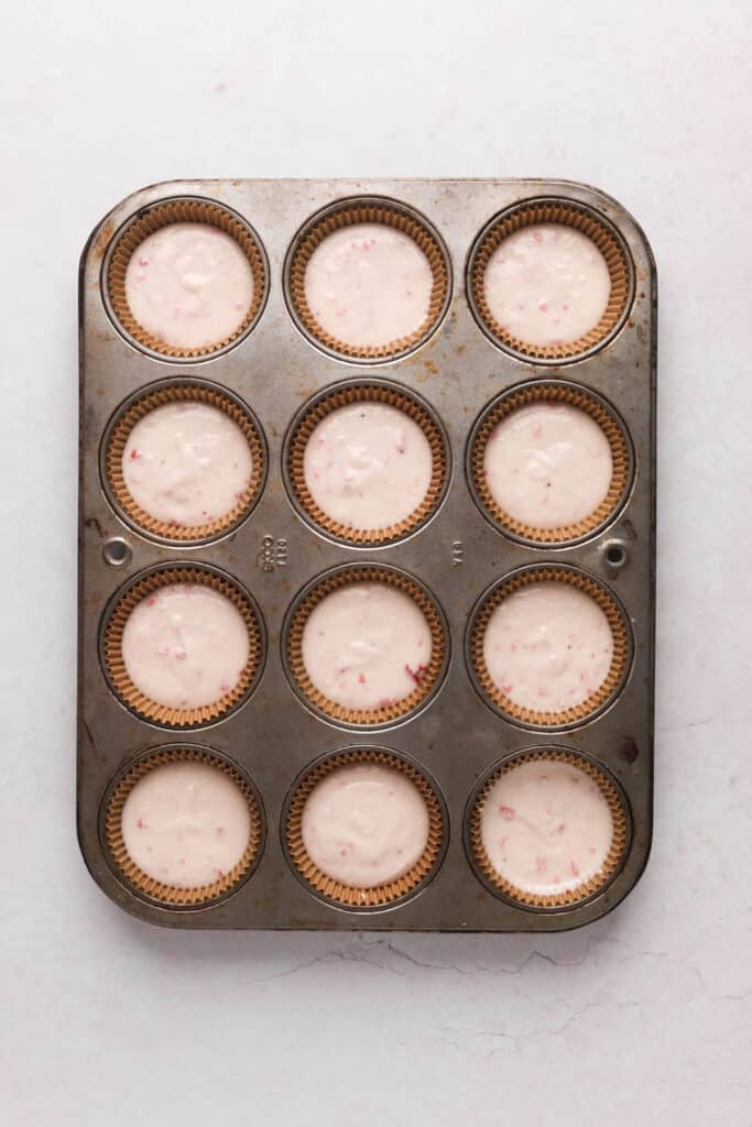 Strawberry cupcake batter divided into cupcake liners in a muffin pan.