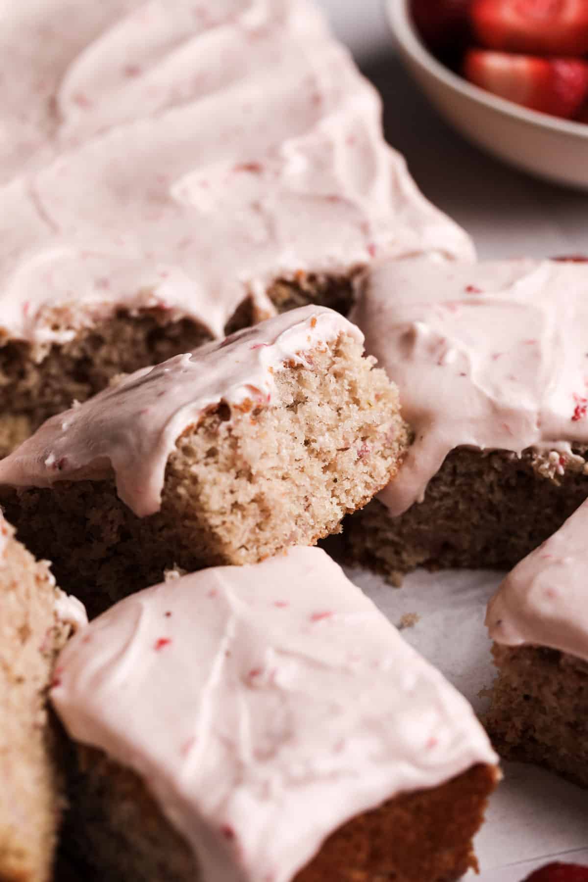 Fresh strawberry sheet cake with strawberry cream cheese frosting on a flat board with square slices out.