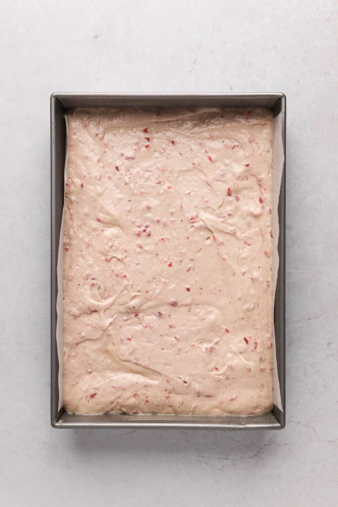 Parchment line 9x13 baking pan filled with strawberry cake batter.