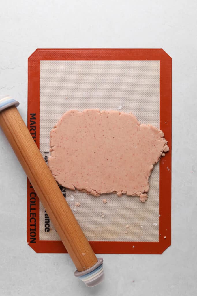 Strawberry shortbread dough rolled on a silicon baking mat with a rolling pin.