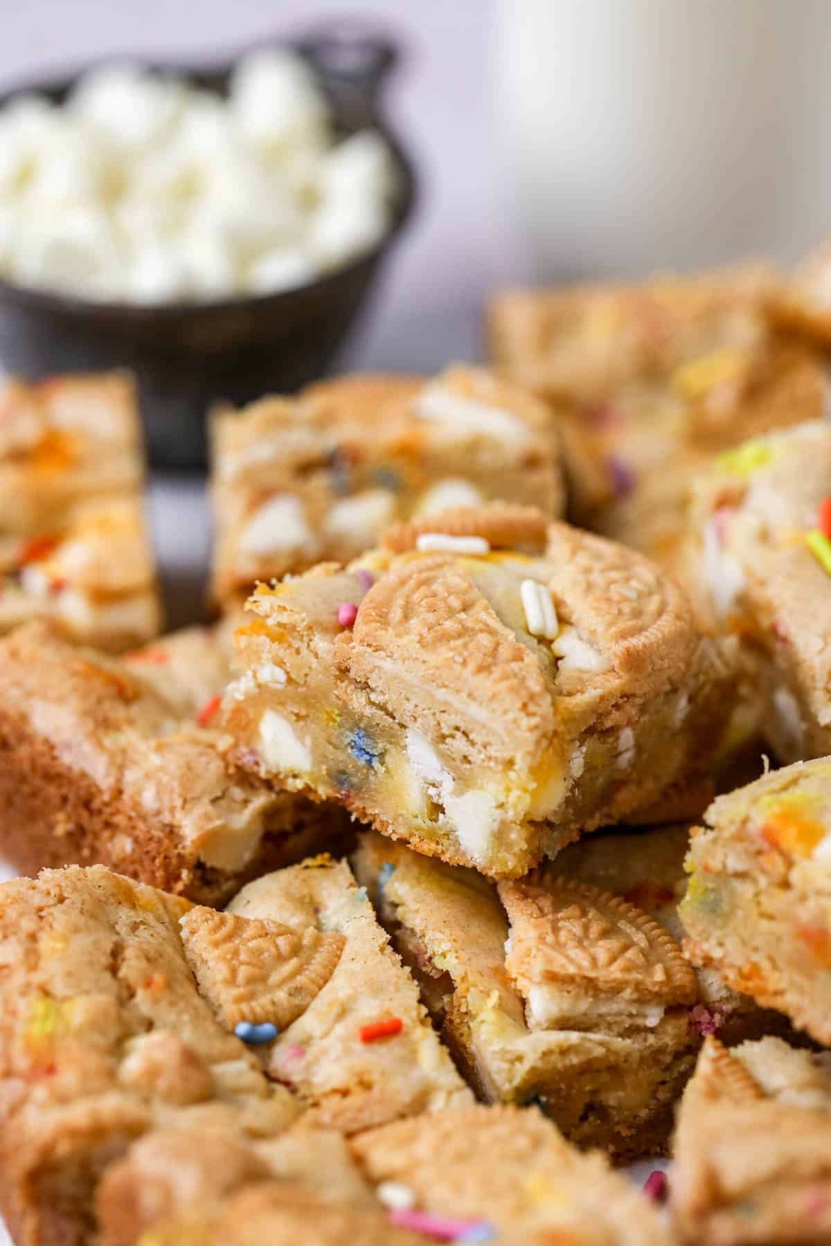 Cut birthday cake blondies stacked in a pile with white chocolate chips in the background.