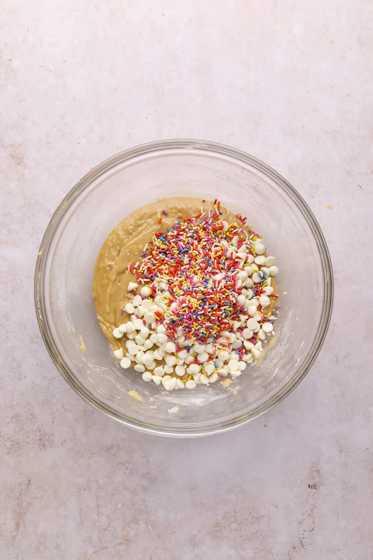 Mixing bowl of birthday cake blondie batter with sprinkles and white chocolate chips on top.