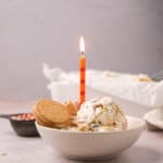 Bowl of scoops of no churn funfetti ice cream with Golden Oreos, sprinkles and a lit birthday candle.