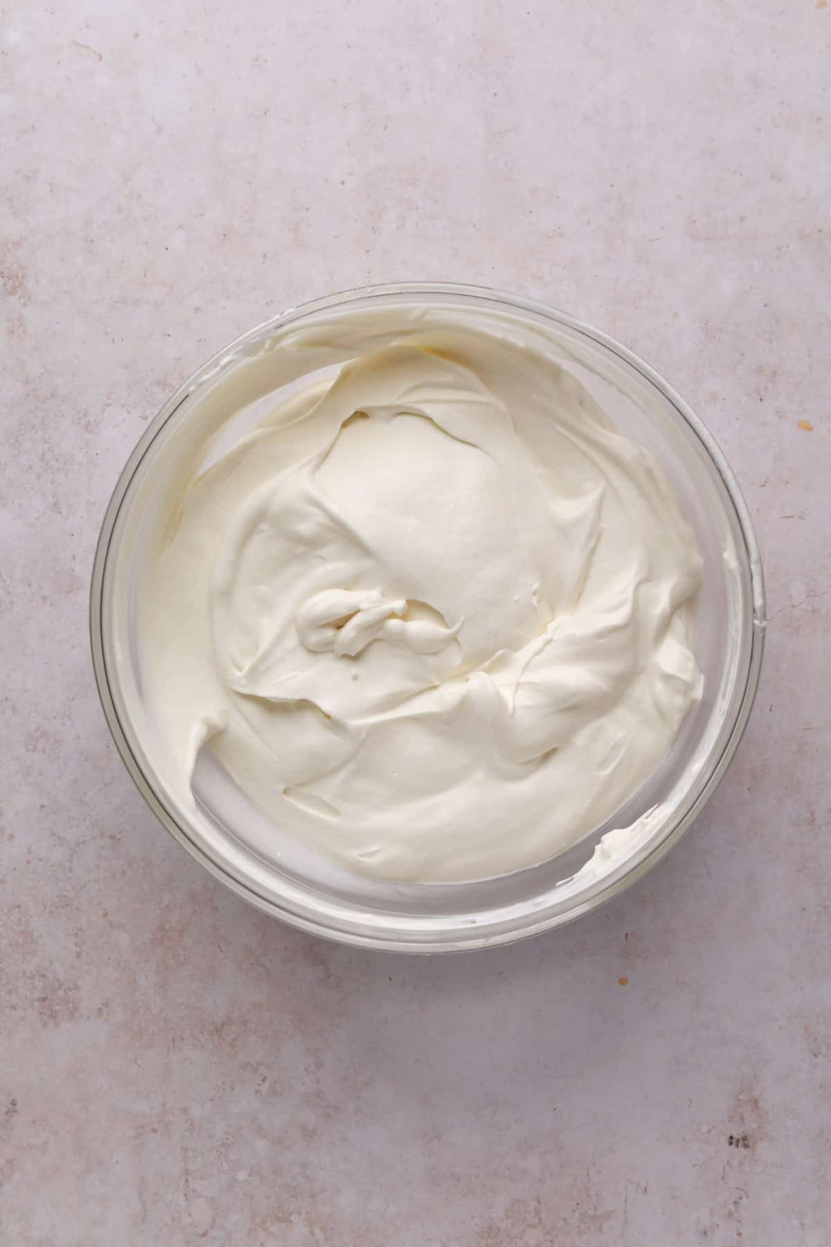 Whipped cream folded into condensed milk and vanilla mixer in a medium bowl for no churn funfetti ice cream.