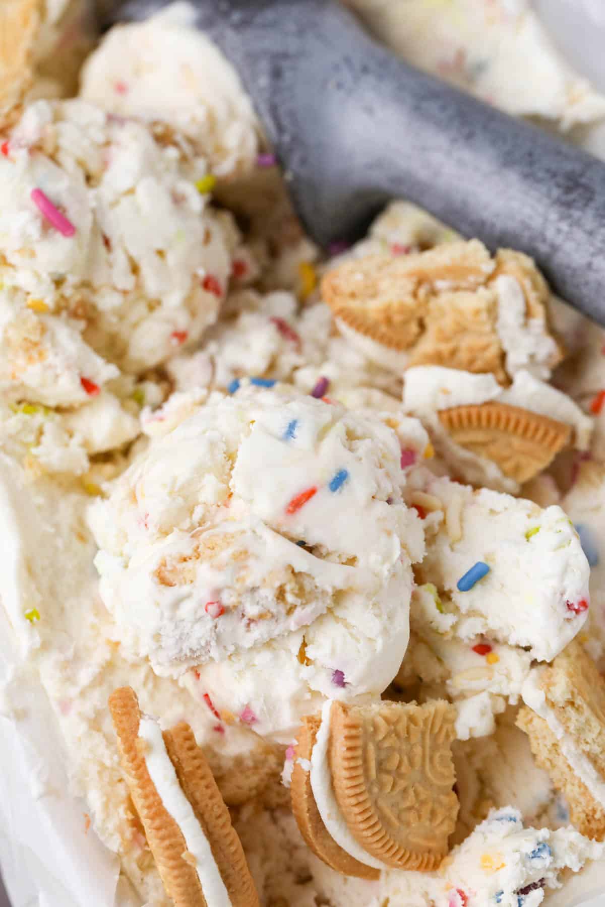 Close up of scoop of frozen no churn Funfetti ice cream in a parchment lined loaf pan with an ice cream scoop, Golden Oreos and sprinkles.